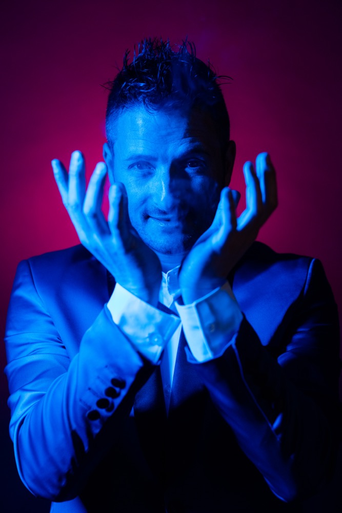Ritratto ravvicinato di Nikola Previti in scena, illuminazione blu drammatica
